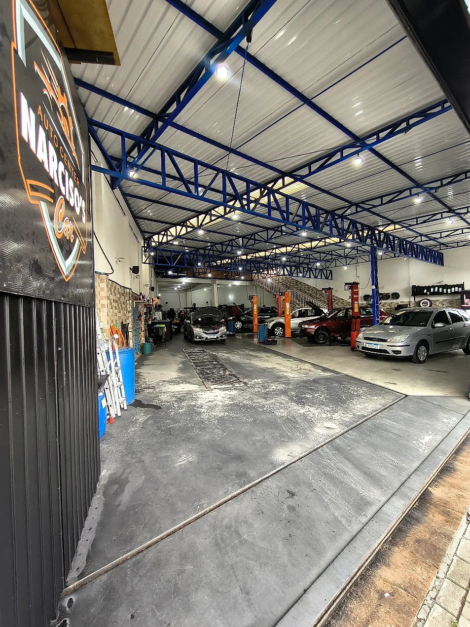 Interior da oficina Narciso's Car visto da entrada, com veículos em atendimento